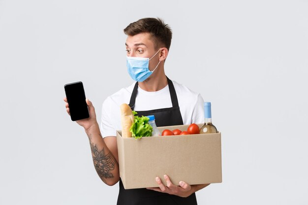 Covid contactless shopping and groceries delivery concept handsome salesman in medical mask suggest ...