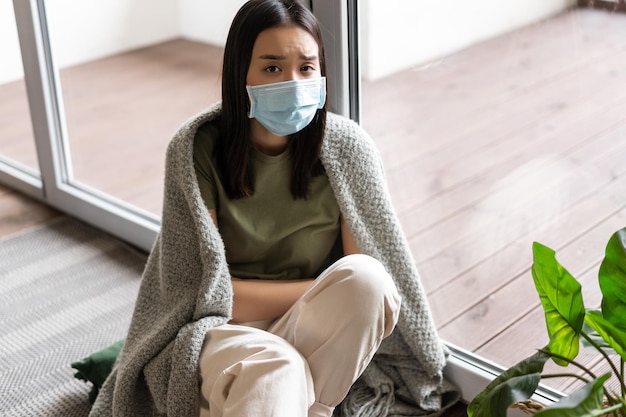 Covid  and pandemic concept sad ill asian girl in medical face mask selfquarantine at home looking o...