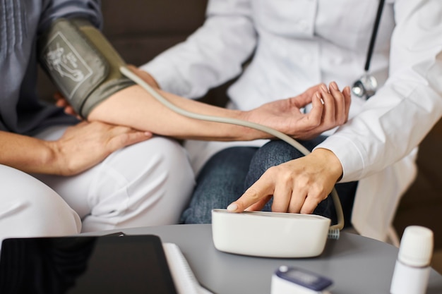 Covid recovery center female doctor checking elder patient's blood pressure with aparatus