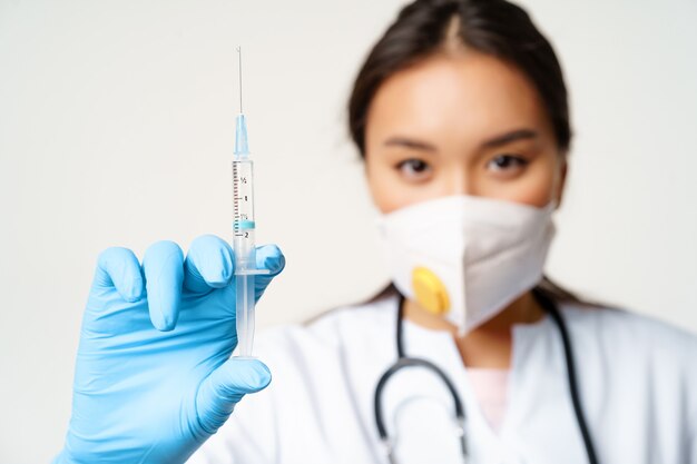 Covid vaccination and quarantine concept asian woman doctor in face respirator showing syringe fille...