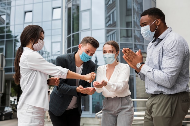 Free photo coworkers disinfecting hands outdoors during pandemic while wearing masks