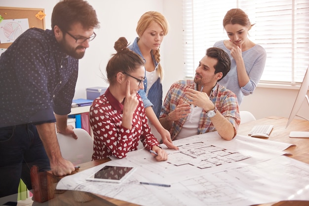 Coworkers at office with architecture plans and a computer