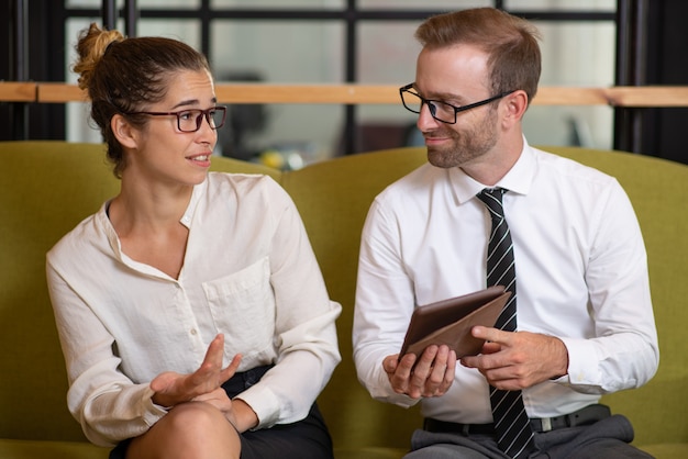 Coworkers using tablet and arguing in office lobby. 