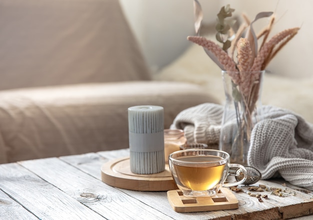 Free photo cozy autumn home composition with a cup of tea, candles and a knitted element on a blurred background of the room interior.