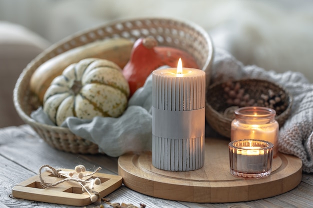 Cozy autumnal composition with burning candles and pumpkins on a blurred background.