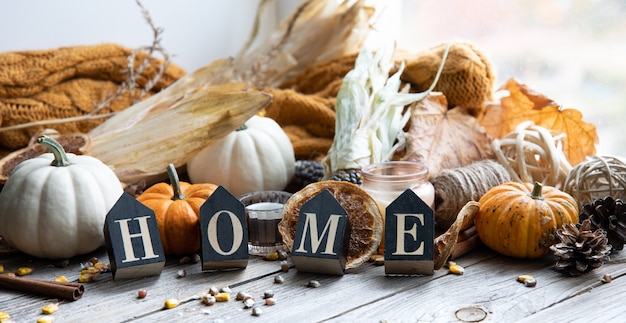 Cozy autumnal composition with decorative word home, candles, pumpkins, corn on a wooden surface in a rustic style.