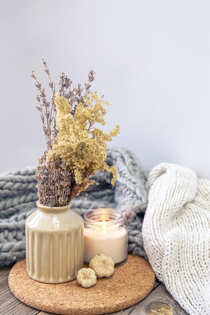 Cozy composition with a vase of dried flowers a candle and a knitted element