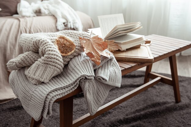 A cozy home composition with a knitted sweater, a book and leaves in the interior of the room.