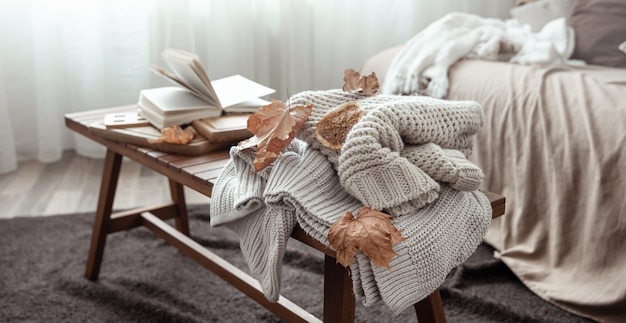 A cozy home composition with a knitted sweater, a book and leaves in the interior of the room.