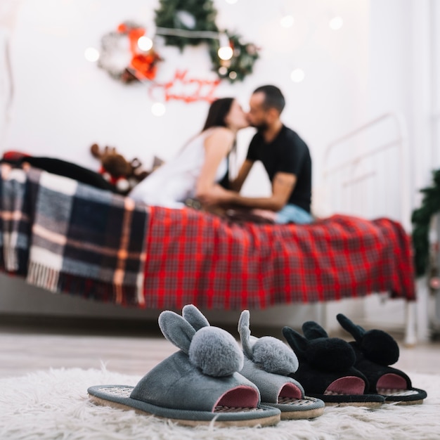 Free photo cozy house shoes on floor near kissing couple on bed