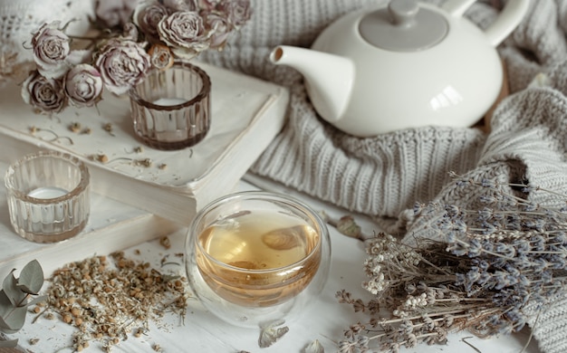 Cozy light still life with candles, a cup of tea, a teapot and dry herbs.