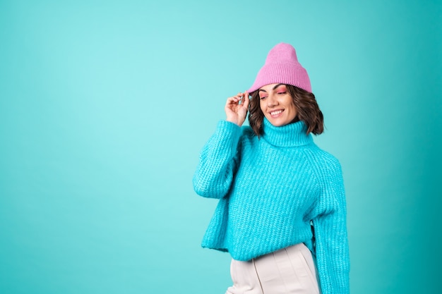 Free photo cozy portrait of a young woman in a knitted blue sweater and a pink hat with bright makeup