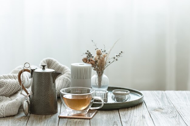 Cozy still life with glass cup of tea, candles and knitted element on blurred background copy space.