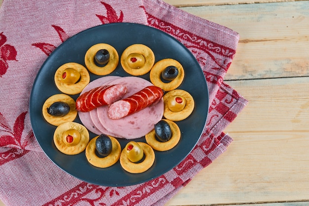 Free Photo cracker rings and slices of sausages with olives on a ceramic plate with pink tablecloth.