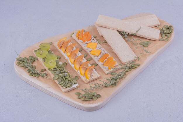 Cracker sandwiches with herbs and fruits on a wooden board