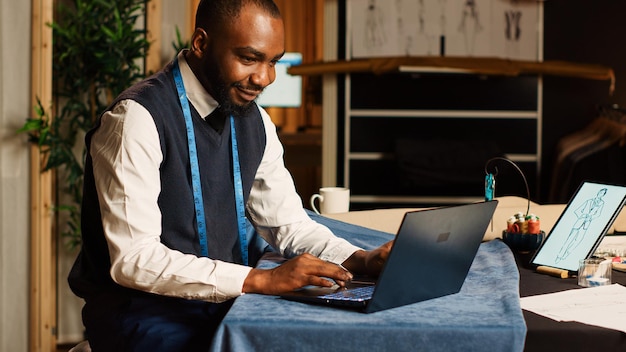 Free Photo craftsman looking for inspiration model on laptop, trying to find design to craft handmade clothing collection. male tailor manufacturing fashion line, checking sketches in workshop.