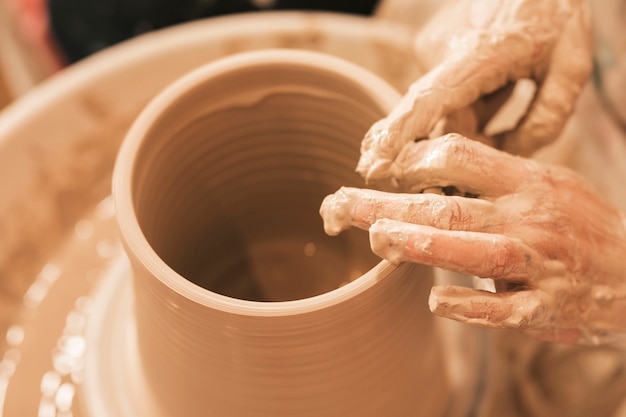 Free photo craftswoman shapes the earthen pot with his hands on pottery wheel