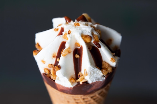 Cream and chocolate ice cream cone with hazelnut and almond on a dark colored background