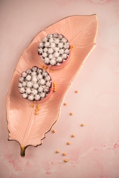 Free photo creamy chocolate cake with berries on pink ceramic leaves on textured backdrop