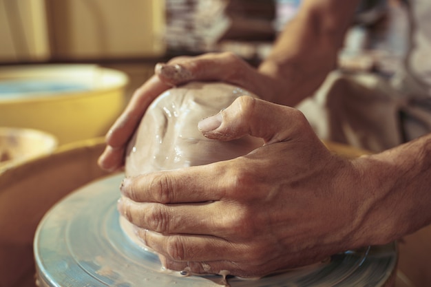 Free Photo creating a jar or vase of white clay close-up. master crock. man hands making clay jug macro. the sculptor in the workshop makes a jug out of earthenware closeup. twisted potter's wheel.