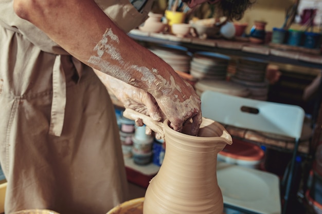 Free Photo creating a jar or vase of white clay close-up. master crock. man hands making clay jug macro.