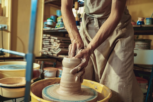 Free photo creating a jar or vase of white clay close-up. master crock. man hands making clay jug macro.