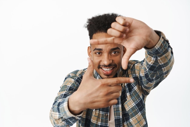 Creative african american male student guy looking through finger frames and smiling amused capture moment taking photo camera imaging something white background