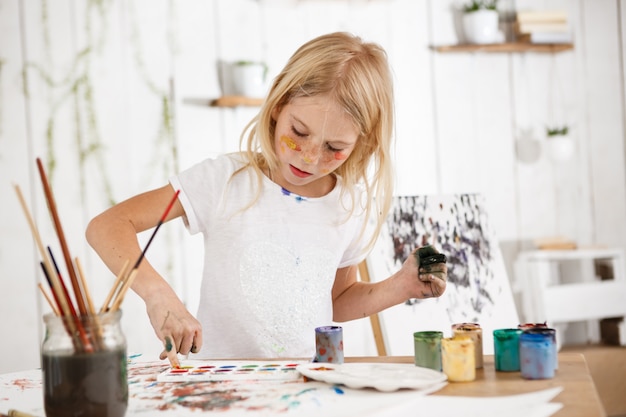 Free photo creative beautiful female child with blonde hair working on her picture in the art room