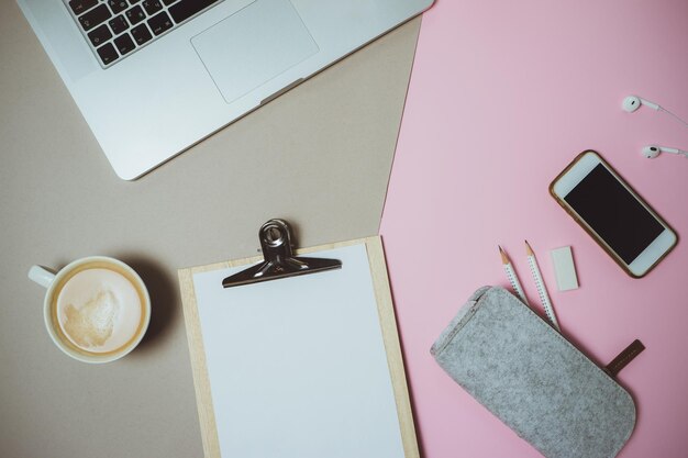 Creative desktop with laptop coffee and stationery on pink and grey table Top view Flat lay