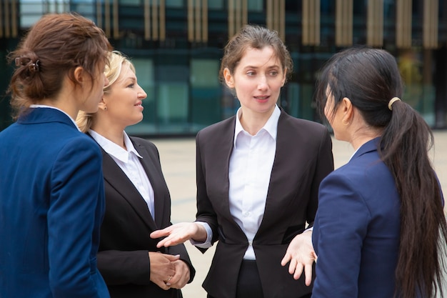 Free Photo creative female business team discussing project outdoors. businesswomen wearing suits standing together in city and talking.