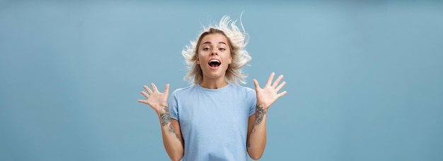 Free photo creative happy and playful beautiful blond girl with tattoos on arms raising palms up opening mouth