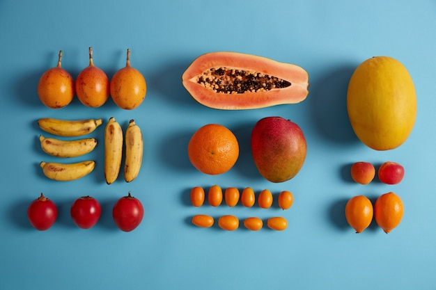 Free Photo creative layout of juicy tropical fruits on blue background. ripe bananas, red fortunella, oranges, peaches, half of papaya, cumquat. exotic fruits for your healthy nutrition. clean eating, vitamins