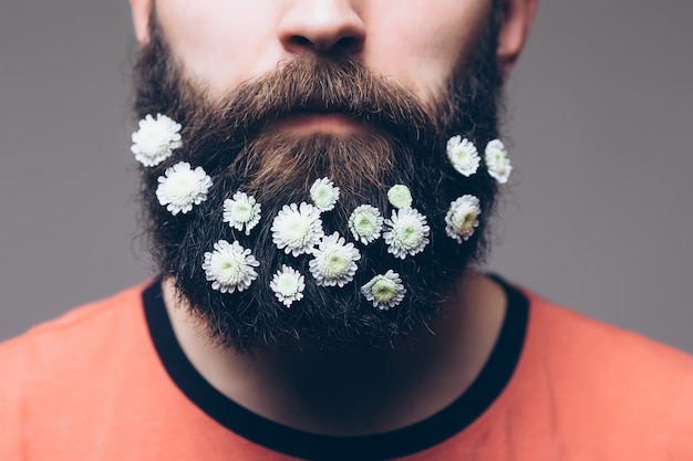 Free photo creative portrait of young beautiful man with a beard decorated with flowers.