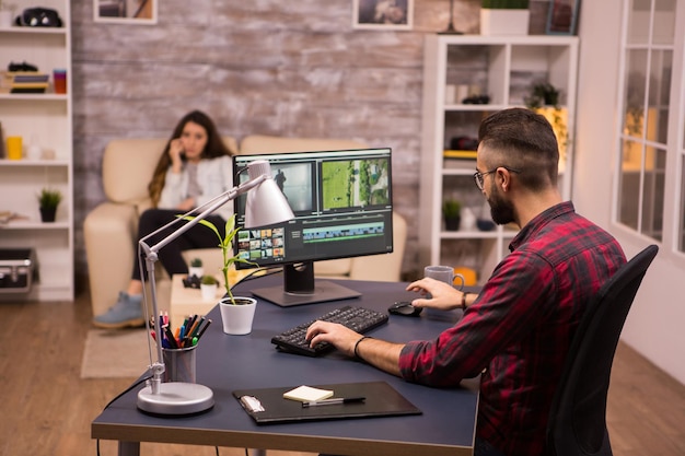 Free photo creative videographer editing a movie on computer from home. girlfriend on sofa in the background