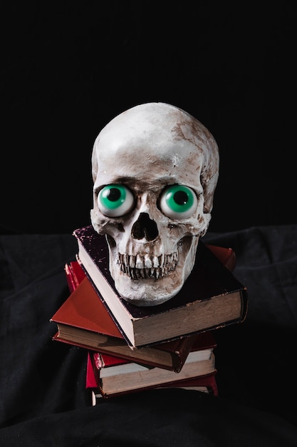 Free photo creepy cranium with funny toy eyes on pile of books