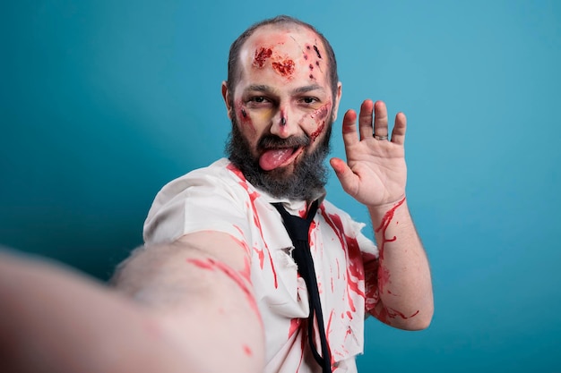 Creepy eerie zombie taking picture on camera, posing in studio and looking dangerous. Brain eating corpse with bloody scars and wounds, horror aggressive monster with apocalyptic look.