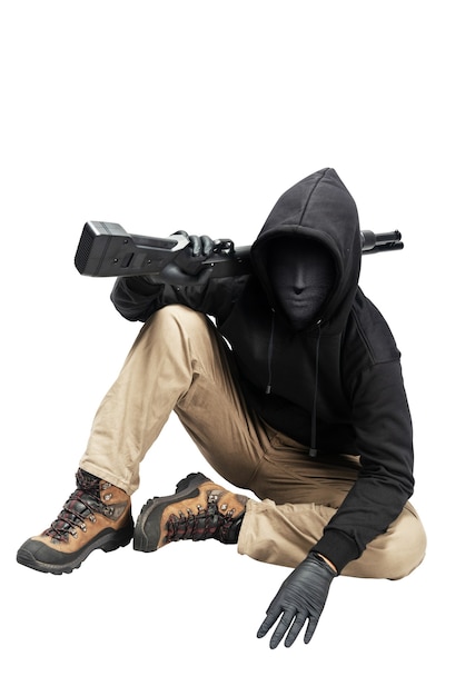 Criminal man in a hidden mask sitting and holding the shotgun isolated over white background