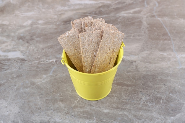 Crispbread falling from overturned yellow bucket, on the marble surface