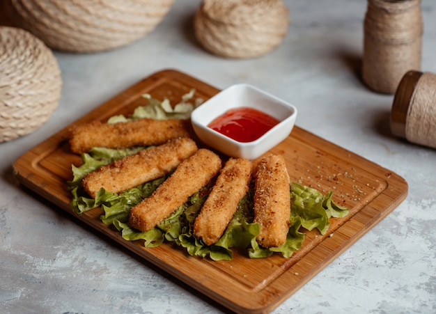 Crispy chicken finger snacks, sticks with ketcup on a wooden board