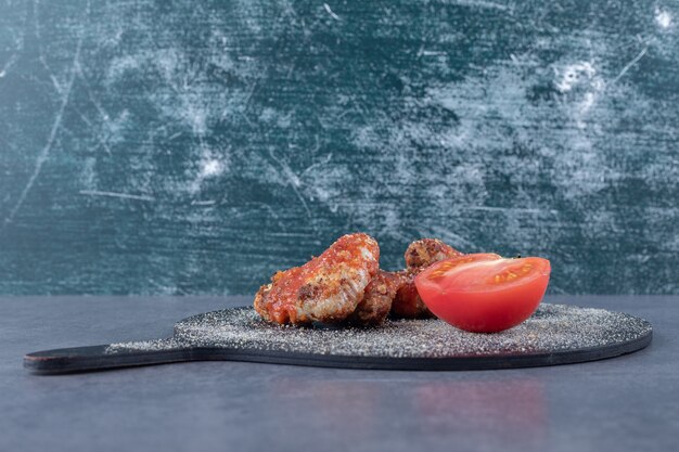 Crispy fried wings and tomato on black board.