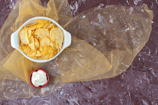 Crispy potato chips and yogurt in a plates on tulle, on the marble table. 