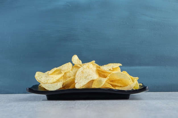 Free photo crispy rippled chips on black plate and striped tablecloth.