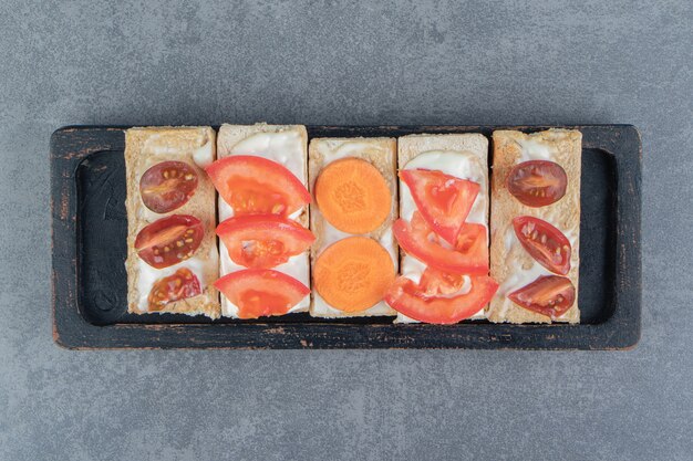 Crispy toasts with tomatoes on wooden board .