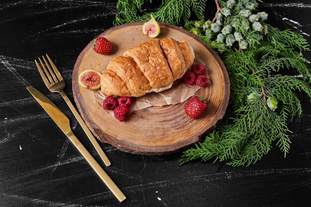 Croissant with berries on wooden platter .