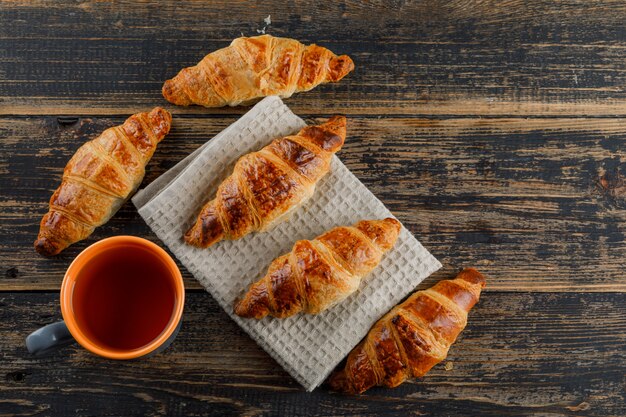 Croissant with cup of tea flat lay on wooden and kitchen towel