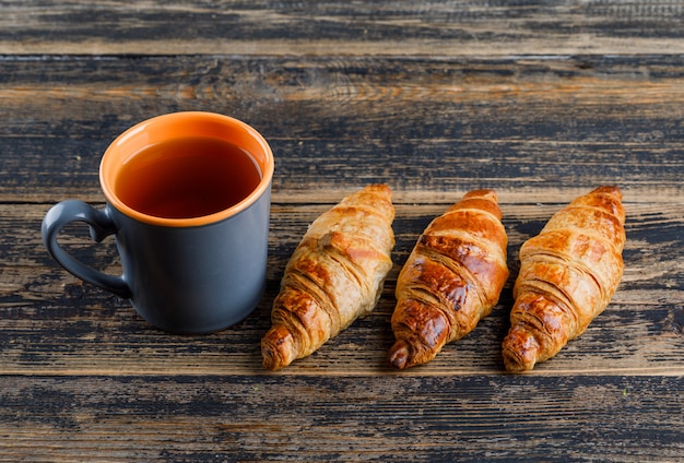 Free photo croissant with cup of tea high angle view on a wooden table