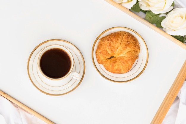 Croissant with cup of tea on wooden tray