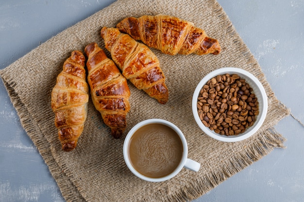 Free Photo croissants with coffee and beans on plaster and piece of sack, flat lay.