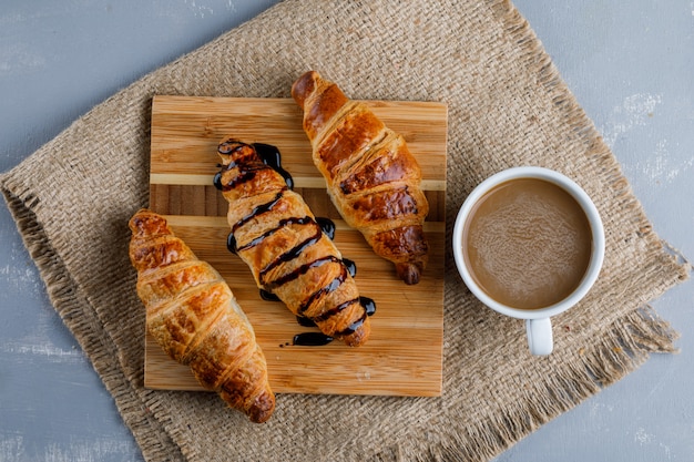 Croissants with coffee, wooden piece flat lay on plaster and piece of sack