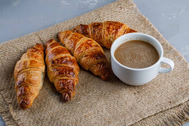 Croissants with cup of coffee on plaster and piece of sack